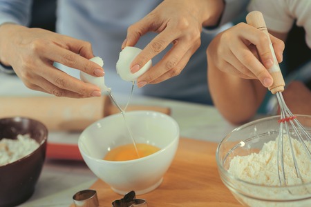 Cooking lesson. Close up of womans hands breaking an egg cooking something with daughterの写真素材