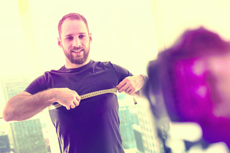 Nice day. Handsome attractive man measuring his muscles while posing in front of the cameraの写真素材