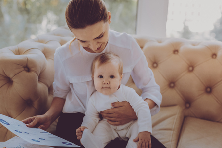Real delight. Appealing smiling mother feeling delighted while holding her little lovely baby daughter at homeの写真素材