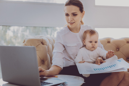 Maternity leave. Fashion designer on maternity leave feeling motivated checking her e-mail while holding little sweet babyの写真素材