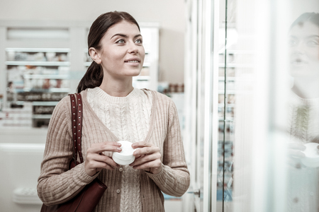 Dark-haired woman with brown leather bag feeling busy while choosing face cream in pharmacyの写真素材
