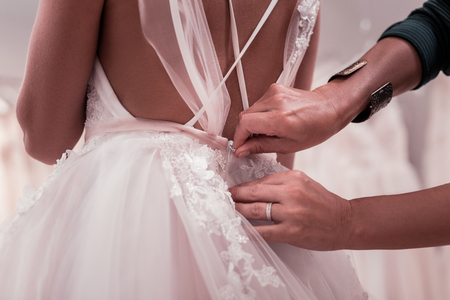 Close up of a wedding dress being fastened by a nice pleasant woman
