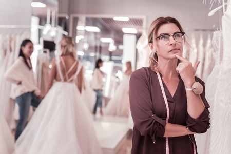Nice thoughtful woman holding her chin while thinking about wedding dressesの写真素材
