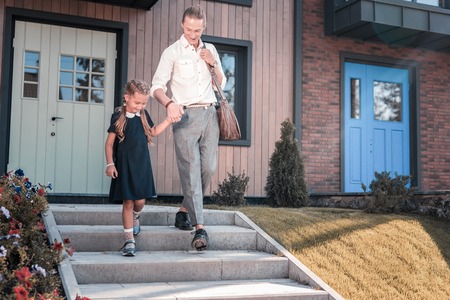Caring loving blonde-haired father holding his cute little daughter while taking her to schoolの写真素材