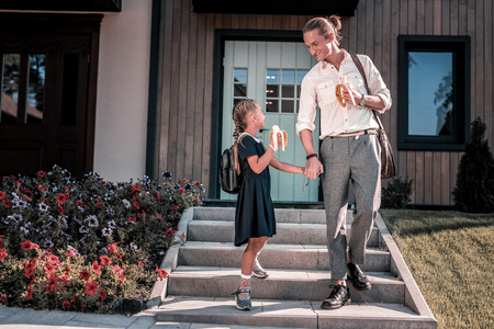 Dark-haired daughter wearing school uniform and backpack talking to fatherの写真素材