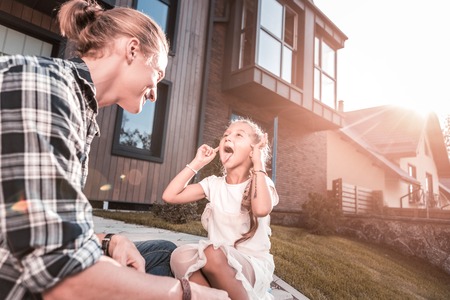 Cute dark-haired girl showing her tongue while having fun with her father outside their houseの写真素材