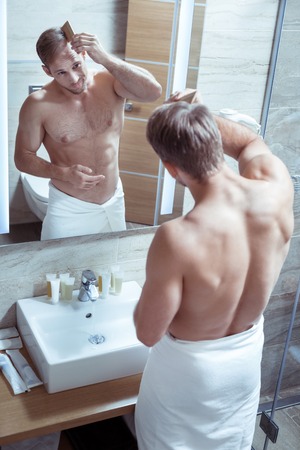Bearded handsome mature man with nice muscle body combing his hair in the morningの写真素材