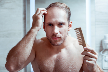Blue-eyed bearded handsome man combing his wet hair after washing it in the shower