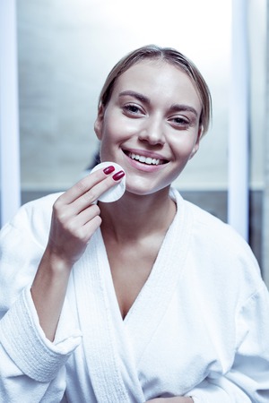 Blonde-haired beautiful woman in bathrobe standing in front of windowの写真素材