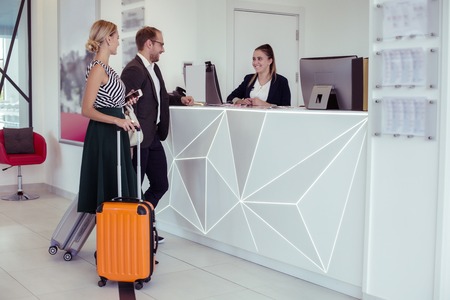 Successful couple of businessmen coming to receptionist in hotel before meetingの写真素材