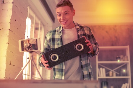 Beaming teenager displaying musical equipment on camera of his mobile phone wearing white t-shirtの写真素材