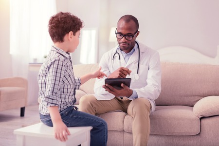 Smart intelligent doctor holding his tablet while talking to the patientの写真素材