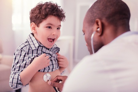 Cute nice boy looking at his doctor while being checked by himの写真素材
