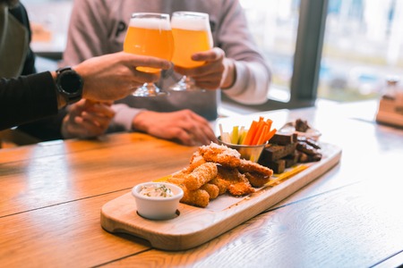 Males snacks. Silhouette of two men that touching glasses while enjoying beer