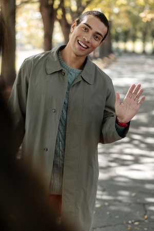 Cheerful brunette keeping smile on his face while looking forward and waving handの写真素材