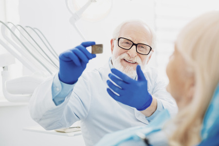 Experienced dentist. Happy male dentist carrying radiography while communicating with patientの写真素材