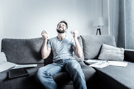 In despair. Irritated bearded man raising arms and making fists while looking upwardsの写真素材