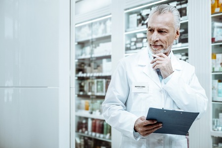 Work with pleasure. Kind mature medical worker keeping smile on his face while looking at shopwindowの写真素材