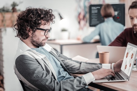 Look attentively. Professional programmer staring at computer while sitting at his workplace