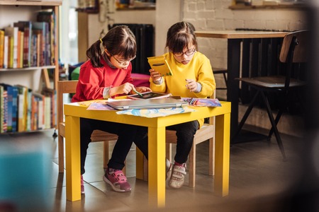 Colorful pencils. Two preschool girls with Down syndrome holding colorful pencils while drawing...