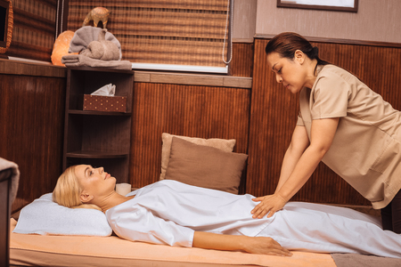 Skilled hands. Serious skilled masseuse performing the massage while working in the spa salonの写真素材