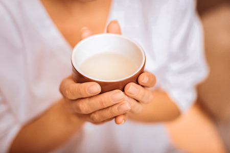 Useful drink. Top view of a cup with herbal tea being in hands of a nice young womanの写真素材