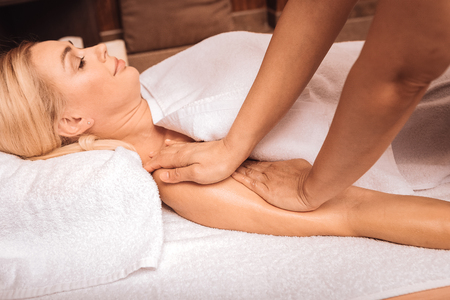 Wonderful feelings. Nice young woman smiling while having her hand massagedの写真素材