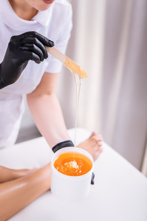 Wax on legs. Professional depilation master putting wax on legs of her client lying in bed near herの写真素材