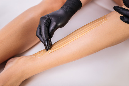 Making sugaring. Master in hair removal wearing black gloves making sugaring for her client lying on bedの写真素材