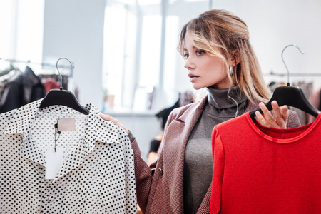 Choosing clothes. Young appealing active fashion blogger choosing new clothes for her videoの写真素材