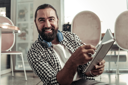 Great mood. Cheerful positive man smiling to you while pointing at his notebookの写真素材