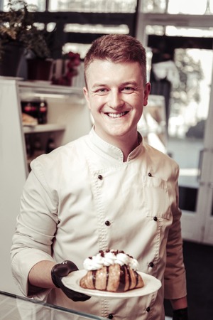 Professional pastry chef. Happy nice man holding a plate with a croissant while working as a pastry...