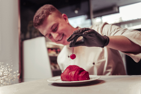 Sweet cherry. Selective focus of a cherry in hands of a nice skilled pastry chef while decorating the croissantの写真素材