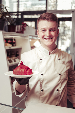 My masterpiece. Cheerful happy pastry chef smiling to you while holding a plate with a croissantの写真素材
