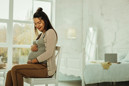 Preparing for becoming a mother. A pregnant woman sitting in her bedroomの写真素材