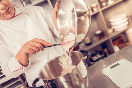 Special cake. Serious nice pastry chef looking into the bowl while putting the ingredients into the big saucepanの写真素材