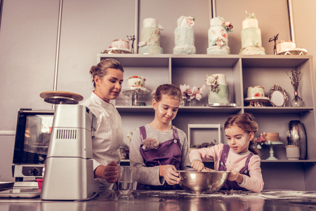 In the cooking academy. Professional female chef standing near the girls while controlling the process of cookingの写真素材