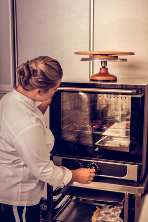 Time to bake. Mice young woman looking at the muffins while setting the temperature in the ovenの写真素材