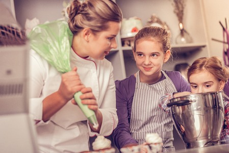 Young cooks. Happy excited girls looking at their mom while helping her to make cupcakesの写真素材