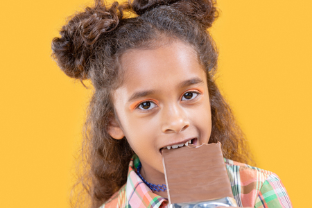 Sweet child. Face of a cute nice afro American girl while eating a chocolate barの写真素材