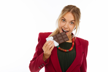 So sweet. Delighted cheerful woman biting a bar of chocolate while enjoying its taste