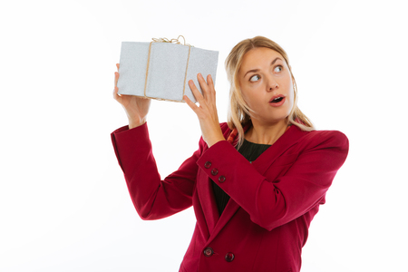 So curious. Nice young woman shaking a gift box while thinking about what is in itの写真素材