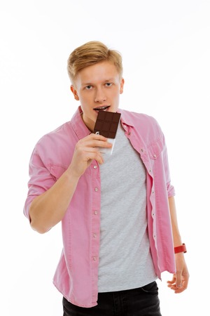 Delicious sweets. Pleasant cheerful man holding a bar of chocolate while