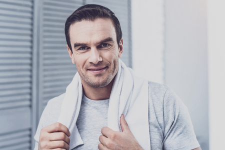 Delighted brunette keeping smile on face while holding towel on neckの写真素材