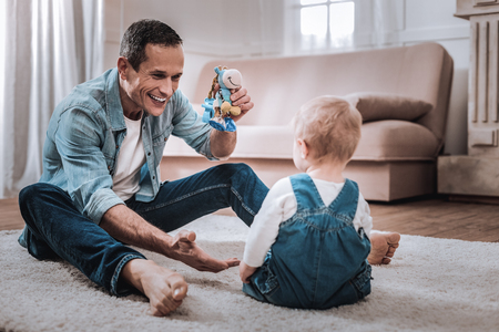 Joyful nice man holding a toy while looking at his childの写真素材