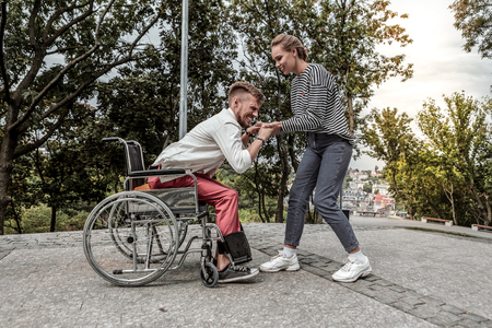 Try again. Young invalid man holding hands of his volunteer while trying to stand upの写真素材