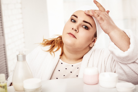 Everyday routine. Plus-size peaceful woman spending her morning in bathroom having morning procedure for skinの写真素材