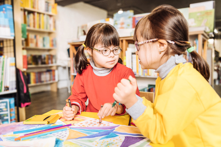 In kids library. Cute appealing sisters with Down syndrome coloring pictures in kids library togetherの写真素材