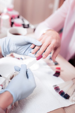 How is it. Nice professional nail master holding an artificial nail while trying on the colourの写真素材