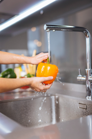 Kitchen. Girl wearing a pink shirt washing vegetables in the kitchenの写真素材